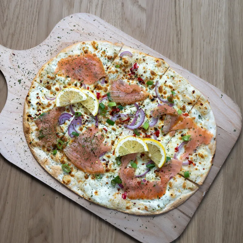 Flammkuchen Kahlo mit Lachs, Zitrone und roten Zwiebeln auf einem Holzbrett