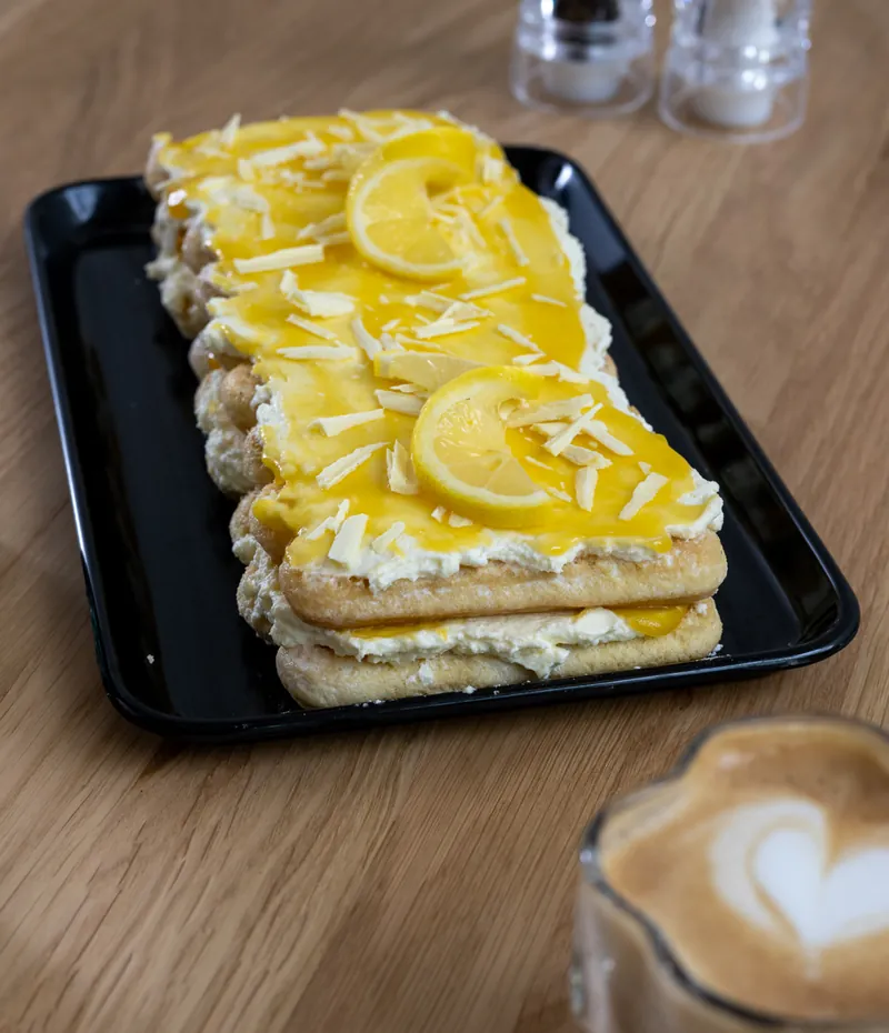 Kuchen mit Zitronenscheiben neben einem Cappuccino mit Latte Art